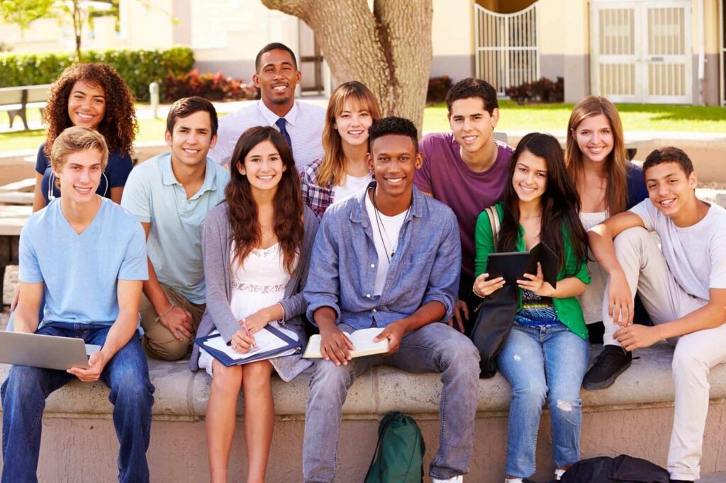 A group of secondary students sits outside under a tree.