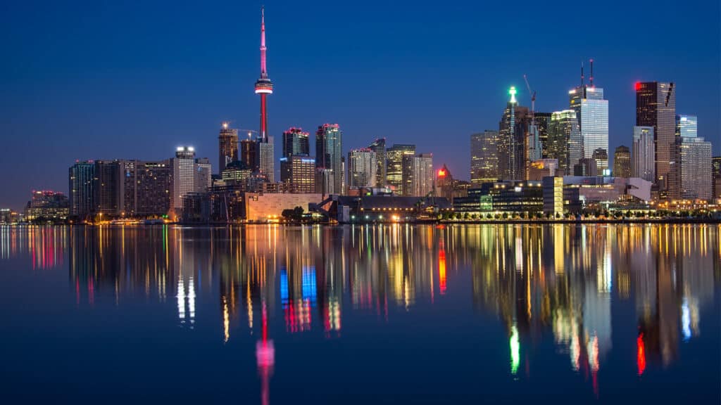 The skyline of Toronto at night with the lights shimmering on Lake Ontario.