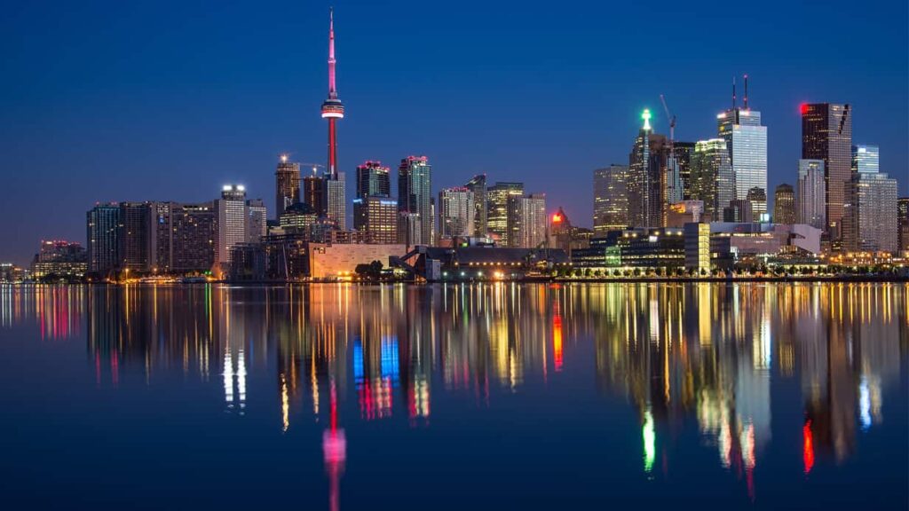 The skyline of Toronto at night with the lights shimmering on Lake Ontario.