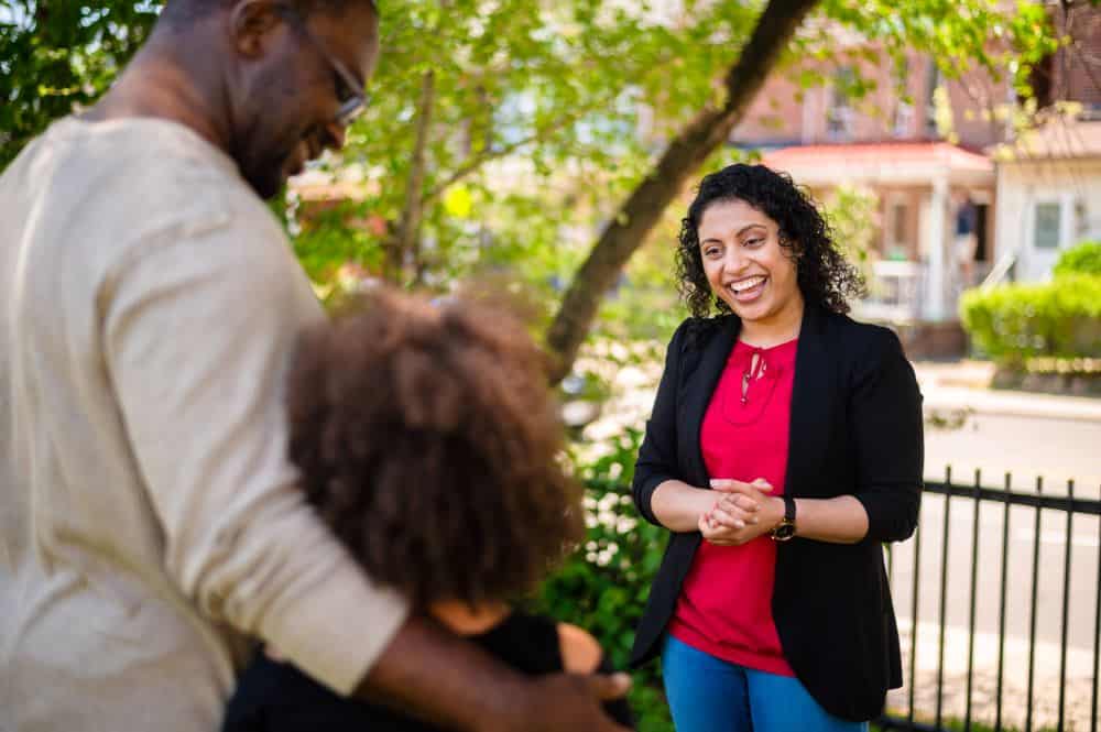 A woman speaks to a father and child in front of a school.