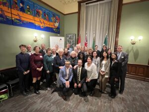 A group of 20-25 members of OPSBA's Board of Directors stand and kneel in a group photo in a historical looking room at Queen's Park in Toronto.