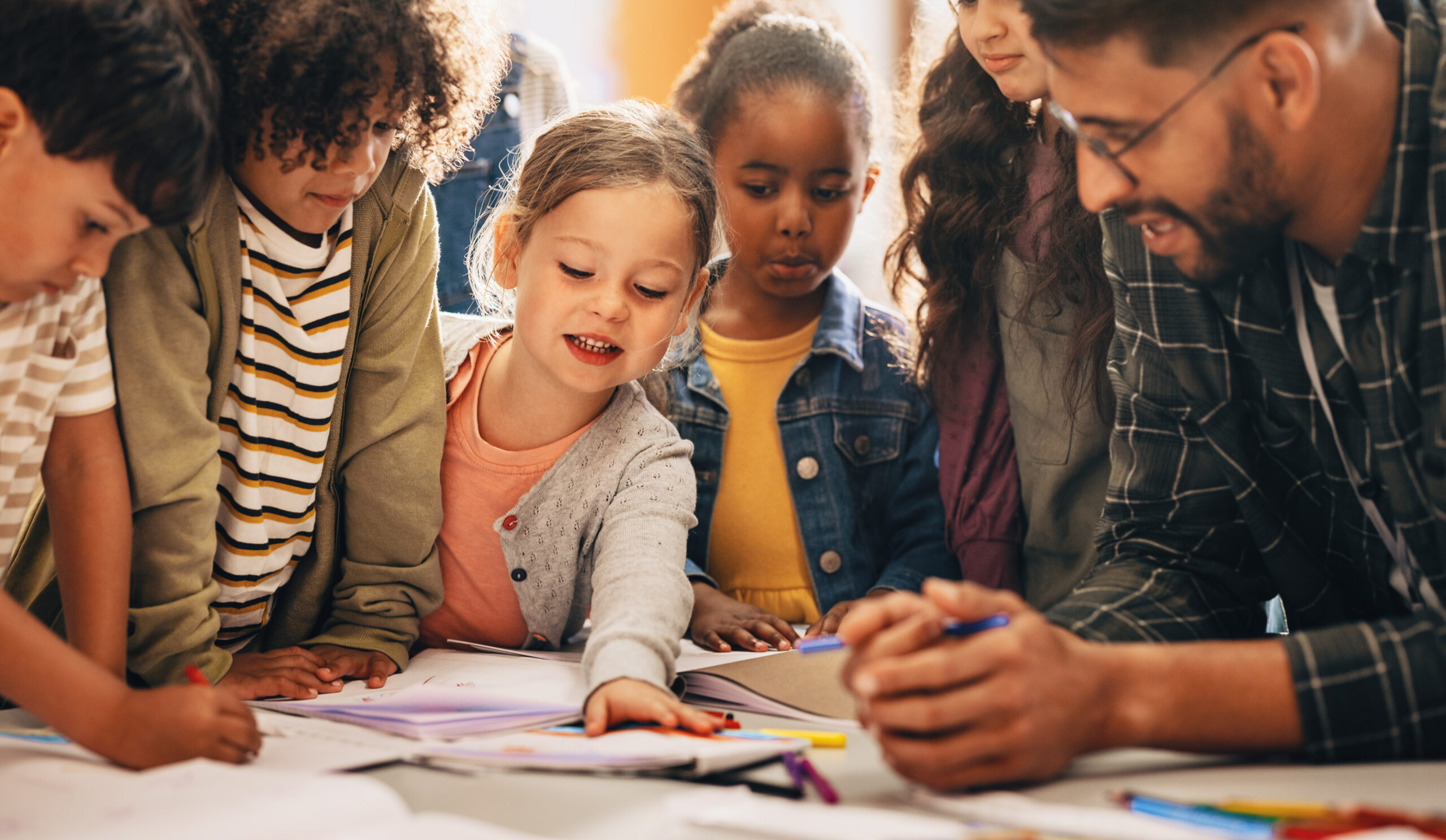 Students doing a creativity project with their teacher in a classroom. Group of primary school children learning how to draw and colour with the help of their educator.